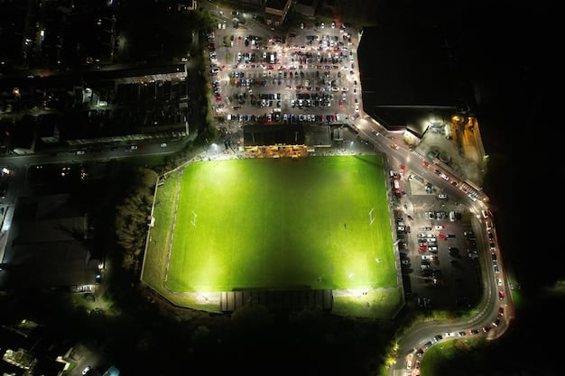 A high-angle shot of a popular La Liga stadium during a night match, filled with cheering fans, with the stadium lights brightly illuminating the pitch where players are actively engaged in a play, and the team benches are visible on the sidelines.