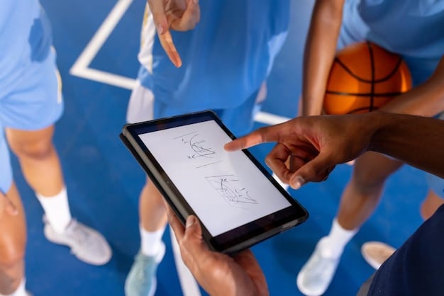 An MLS coach reviewing data on a tablet during a training session. Players are seen running drills in the background. The tablet displays real-time performance metrics.