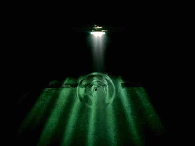 Close-up of a soccer ball with the Champions League logo on a lush green field, slight rain in the background with stadium lights shining brightly